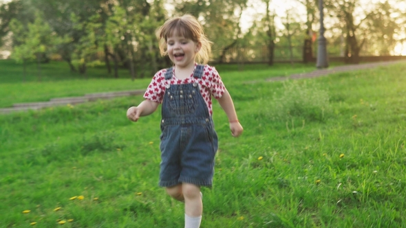 Happy Little Girl Running on Green Grass at Sunset in Sunny Summer Day