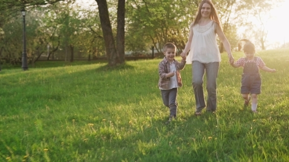 Happy Mother and Kids Holding Hands Running Together on Lawn at Sunset