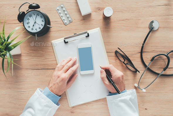 Male doctor writing notes on clipboard paper during medical exam - Stock Photo - Images
