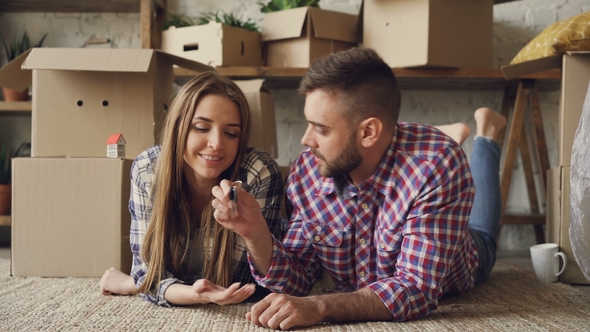 Young Cute Couple in Casual Clothes Is Lying on Floor of New Apartment, Guy Is Giving Keys alt