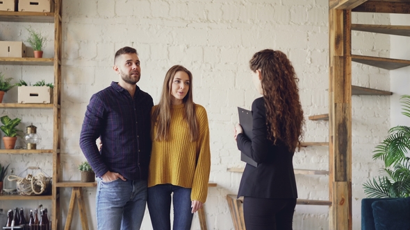 Attractive Couple Is Discussing Real Estate Deal with Female Realtor Standing Inside Beautiful House alt