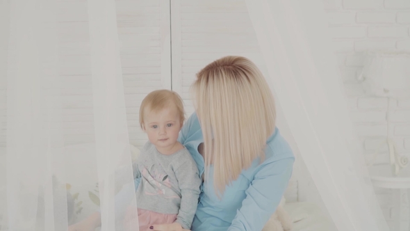 Young Mother Kisses Her Beautiful Daughter on the Bed. Happy Family.