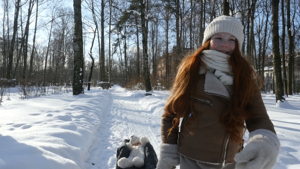 Red-Haired Little Girl Walks on Winter Park at Sunny Day and Sledding Her Toy