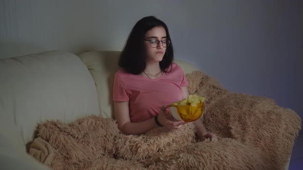 Brunette Pretty Girl with Glasses Eating Potato Chips and Watching Tv at Home