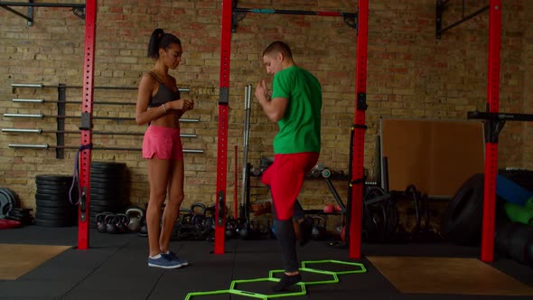 Fitness Trainer Showing Cardio Workout to Black Fit Female Using Agility Ladder alt