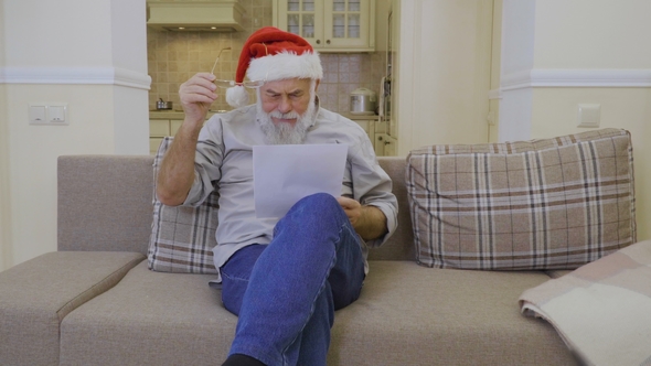 Senior Man in Santa's Hat Reads Family Wish List on Christmas alt