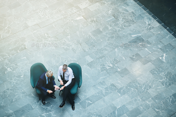 Two mature businessmen talking together in an office lobby - Stock Photo - Images
