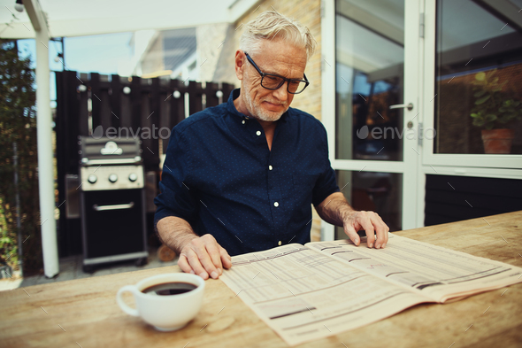 Smiling senior man reading a newspaper on his patio Stock Photo by UberImages
