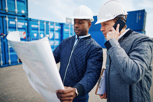 Engineers standing in a freight yard discussing building plans - Stock Photo - Images