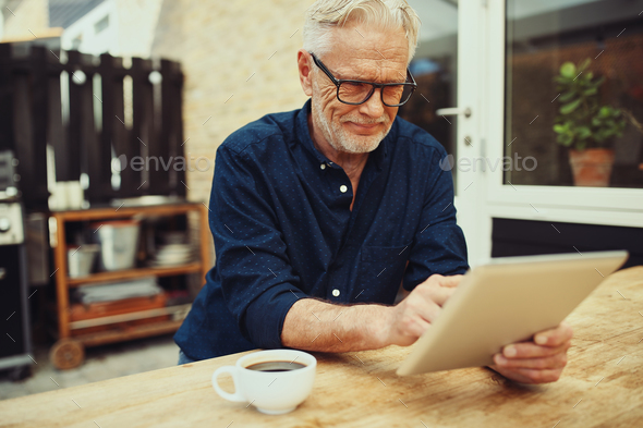 Smiling senior man drinking coffee and using a digital tablet - Stock Photo - Images