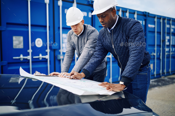 Two engineers discussing building plans together in a freight yard - Stock Photo - Images
