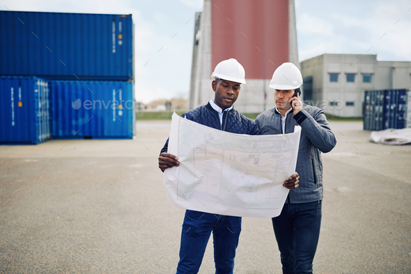 Engineers standing in a shipping yard discussing building plans - Stock Photo - Images
