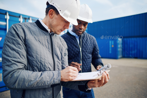 Two engineers standing in a commercial shipping yard tracking containers - Stock Photo - Images
