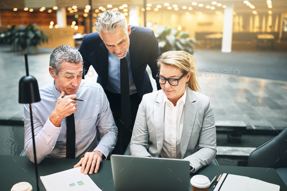 Mature businesspeople talking together over a laptop in an office - Stock Photo - Images