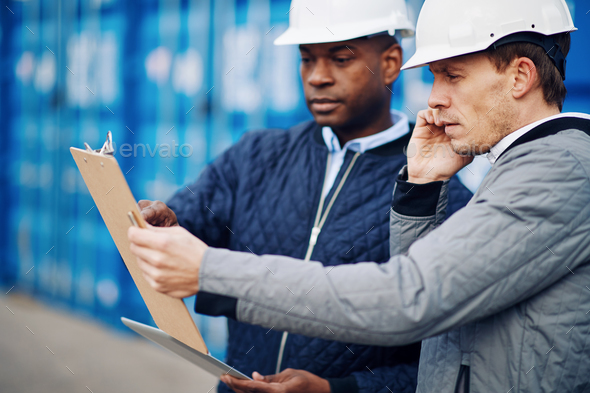 Engineers discussing an inventory together in a commercial freight shipyard - Stock Photo - Images