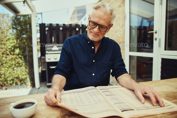 Content senior man reading a newspaper at his patio table - Stock Photo - Images