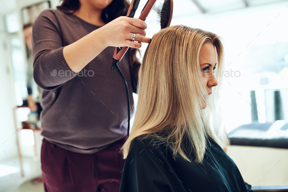 Young woman getting her hair straightened at the salon Stock Photo by UberImages