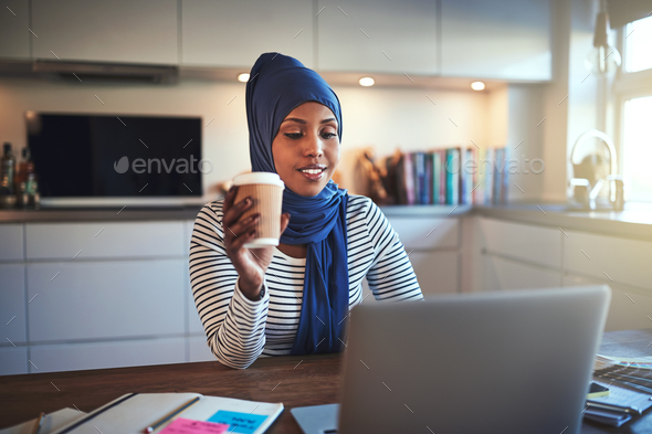 Young Arabic woman drinking coffee and working online at home - Stock Photo - Images