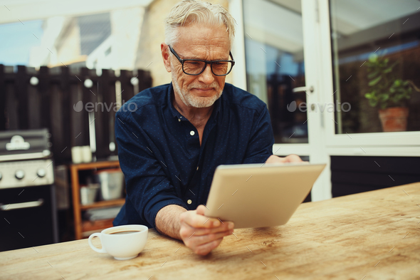 Smiling senior man holding a tablet and drinking coffee outside - Stock Photo - Images