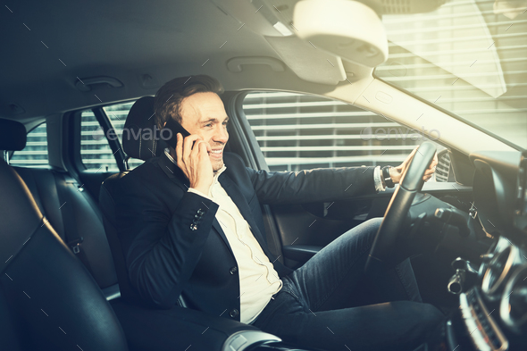 Smiling businessman talking on a phone in his car - Stock Photo - Images