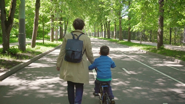 Little Boy on a Bicycle with Mom Walking in the City Park