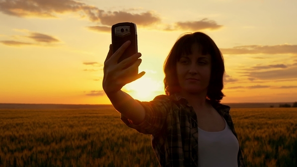 Young Girl Making Herself on a Beautiful Sunset Against a Wheat Field Background alt