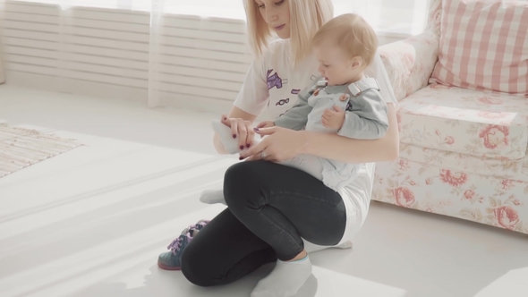 Young Mother Put on Shoes To Her Lovely Baby. Happy Family.