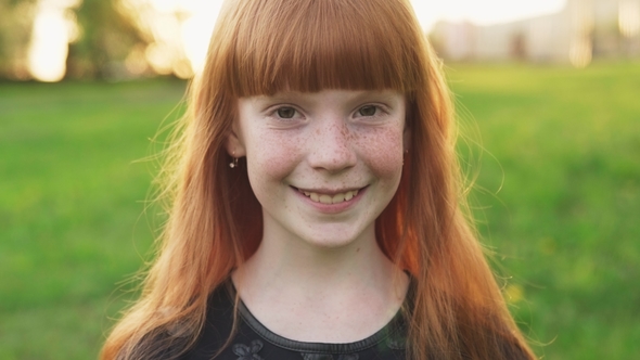 Little Beautiful Redhead Girl with Freckles Smiling and Looking at Camera
