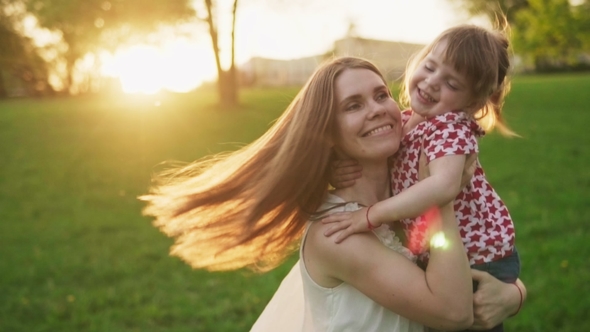 Happy Mother Hugs Adorable Little Daughter and Whirls with Her in Sunny Park