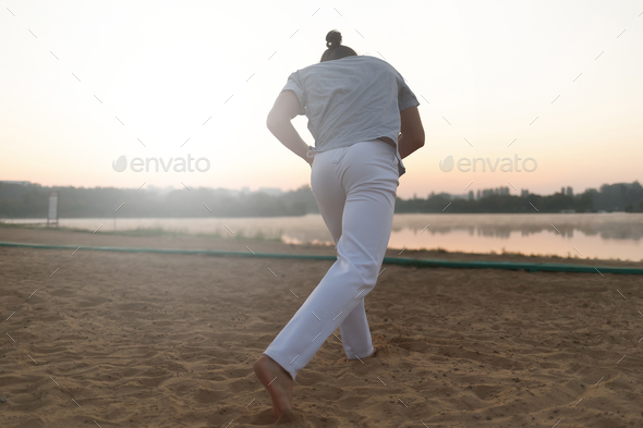 Athletic capoeira performer making movements on the beach - Stock Photo - Images