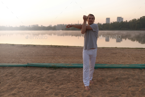 Casual athletic man stretching on the beach while workout. - Stock Photo - Images