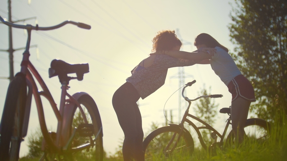 Girls-cyclists Keep Each Other and Warm Up in Pakr, Next To Their Bicycles, Summer Sunny Day alt