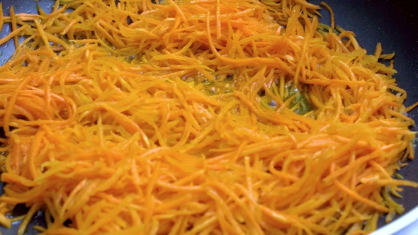 Grated Carrots Are Fried in a Frying Pan on Oil.
