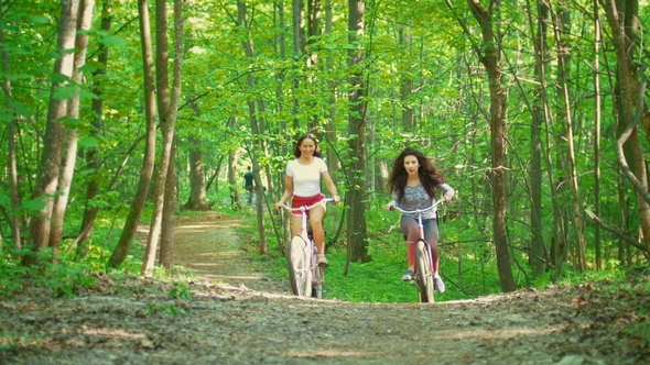 Walking on Bicycles in the Green Forest Two Girls Climb the Path To the Hill , Sunny Day alt