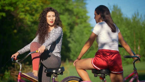 Two Young Cyclists Communicate and Laugh on a Cycling Trip in the Park, on a Sunny Summer Day alt