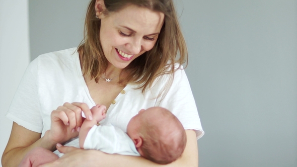 A Woman Is Holding a Newborn Baby in Her Arms. The Child Looks at His Mother and Smiles with a alt