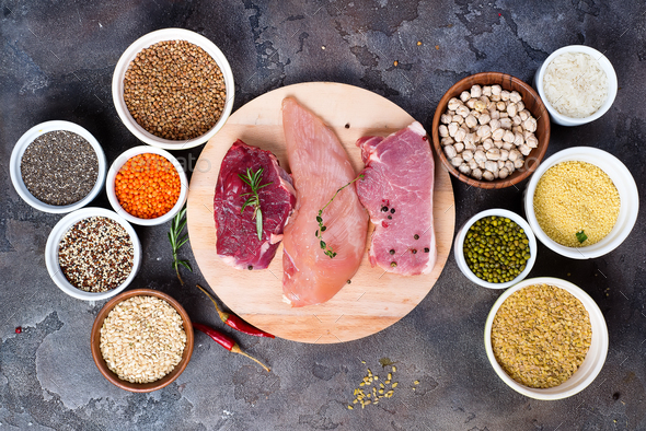 Raw food beef meat and chicken breast with cereals in bowl on stone dark background, flat lay - Stock Photo - Images