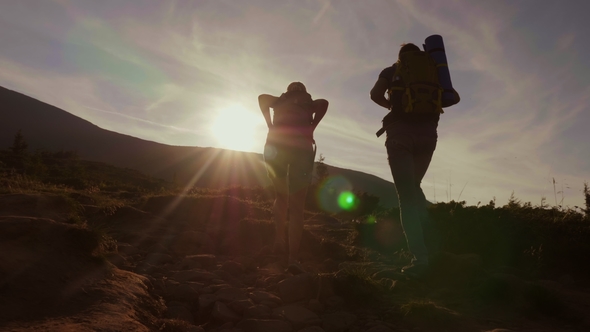 Climbing the Mountain at Dawn. Two Tourists Climb Up the Mountain Path in the Sun alt