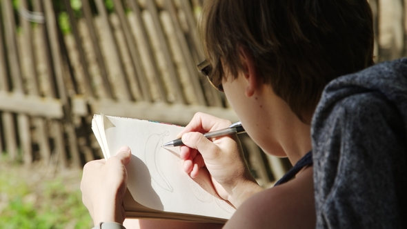 Girl Artist in Sunglasses Draws Sketches in Notebook alt