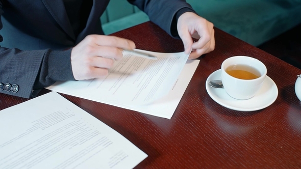 Hands of Businessman Reading Contract in the Cafe.