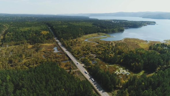 Cars Are Going By the Road Throught the Forest and Bogs Near the Riverside. alt