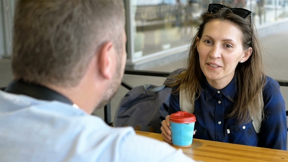 Young Woman Listens Attentively and Looks at Her Boyfriend Sitting in a Cafe. Blue Cup for Coffee on