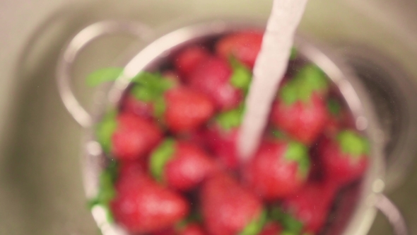 A Stream of Water Pours into a Colander with Strawberries