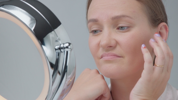 Caucasian Woman with Mirror with Ring Light with No Makeup Look Examine Her Skin and Makes Facial