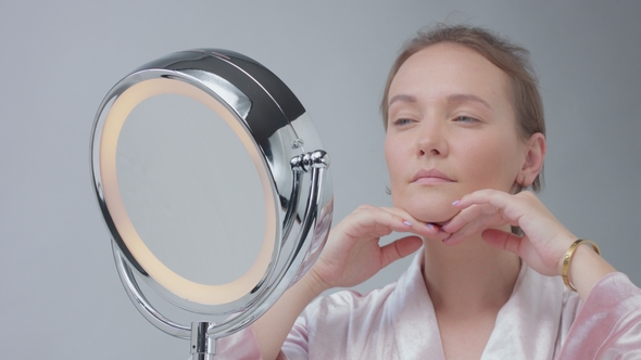 Caucasian Woman with Mirror with Ring Light with No Makeup Look Examine Her Skin and Makes Facial