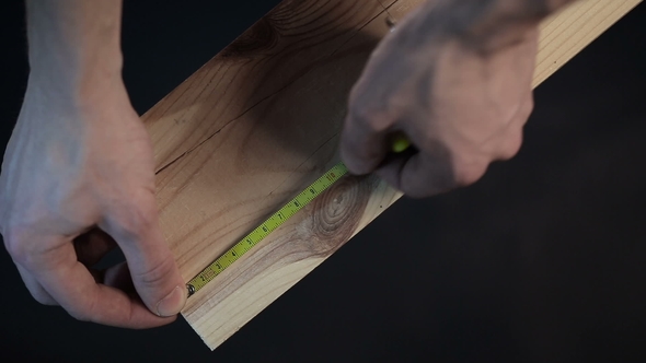 Hands of Carpenter Measuring a Plank with Measuring Tape