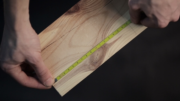 Hands of Carpenter Measuring a Plank with Measuring Tape