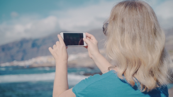 Woman with a Smartphone Makes Photos on the Beach