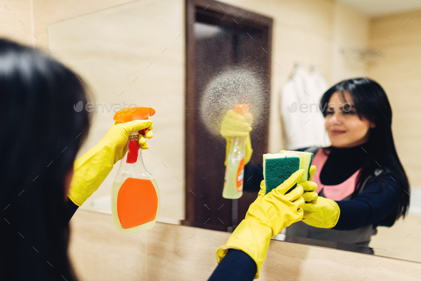 Housemaid cleans the mirror with a cleaning spray - Stock Photo - Images