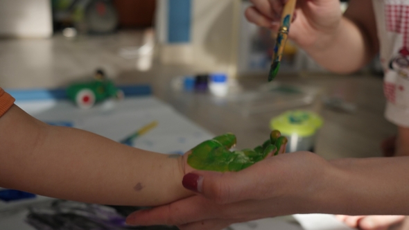 Woman Paints with Brush on Baby Hand for Making Green Handprints.  Shot alt
